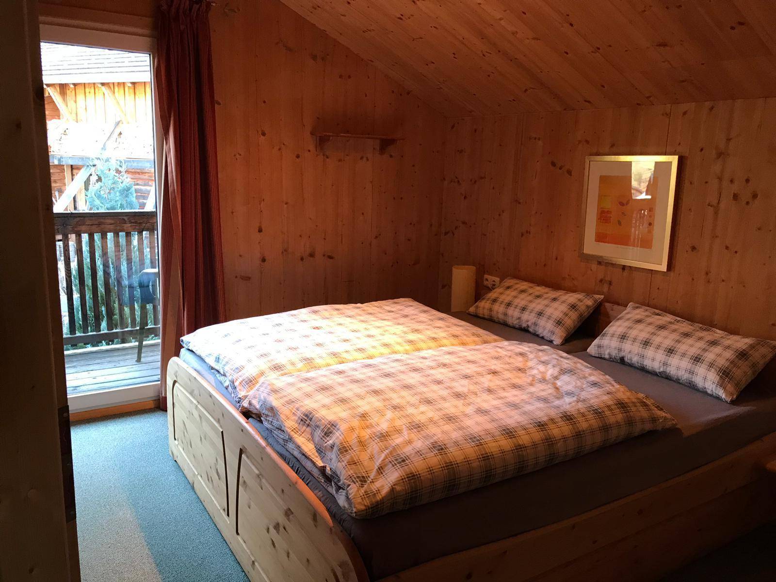 Schlafzimmer mit Holzvertäfelung, Doppelbett und Balkonzugang, unter einem Dachschrägen.