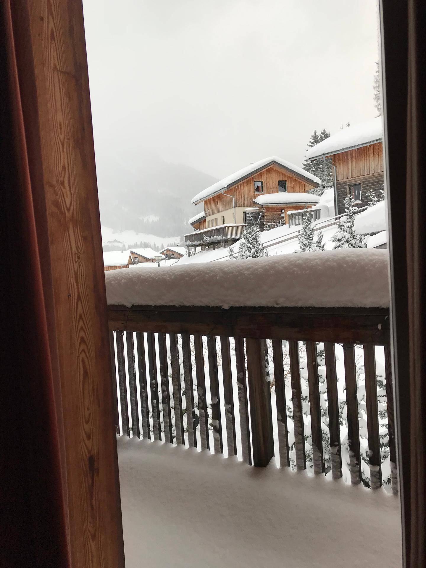 Winterlicher Ausblick vom Balkon auf schneebedeckte Häuser und Bäume in der Ferne.