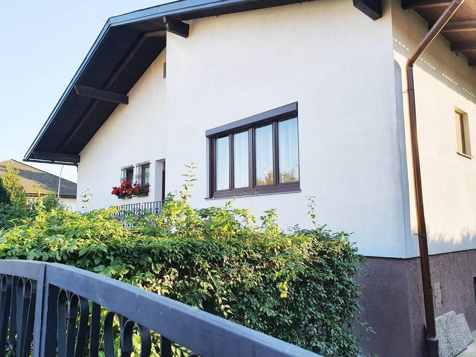 Vorderansicht des Hauses mit weißer Fassade, braunen Fenstern und einem grünen Zaun.