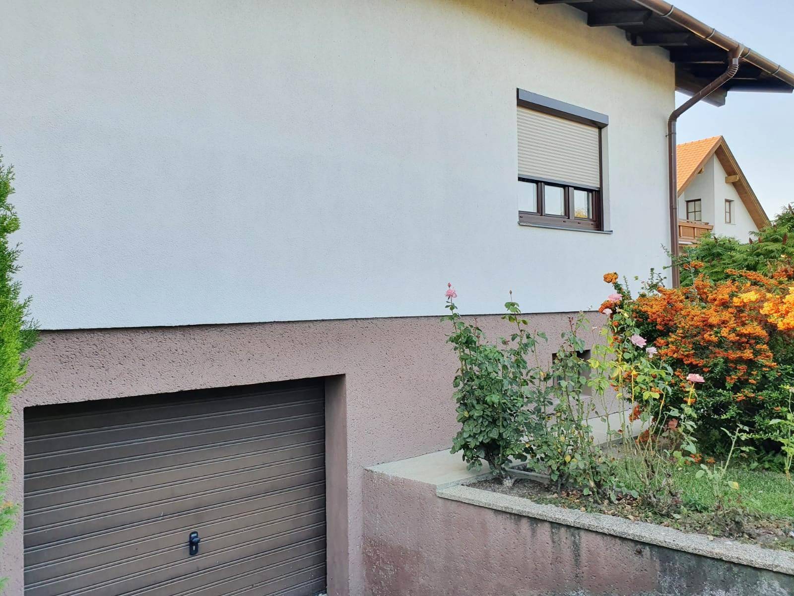 Seitenansicht des Hauses mit Garage im Untergeschoss und einem Fenster mit Rollladen.