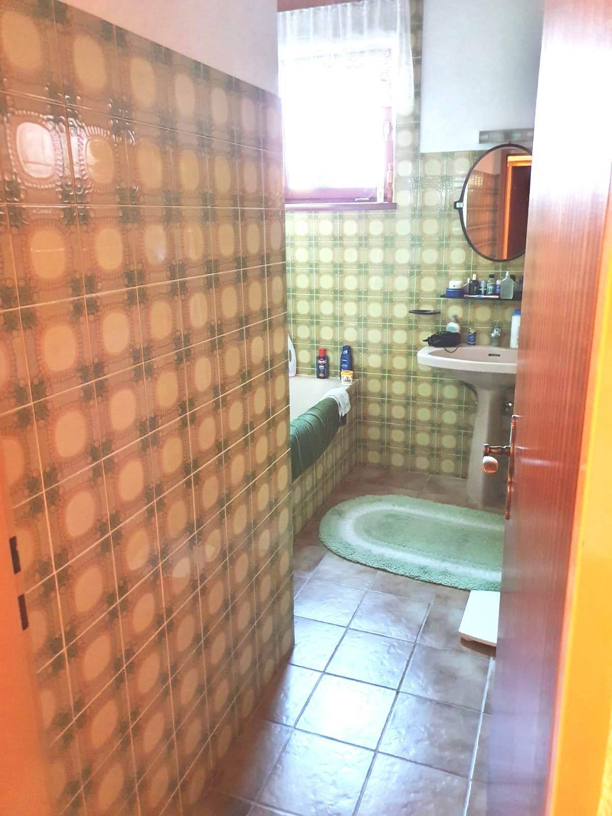 Badezimmer im Stil der 80er Jahre mit grünen Fliesen, Badewanne, Waschbecken und Spiegel.