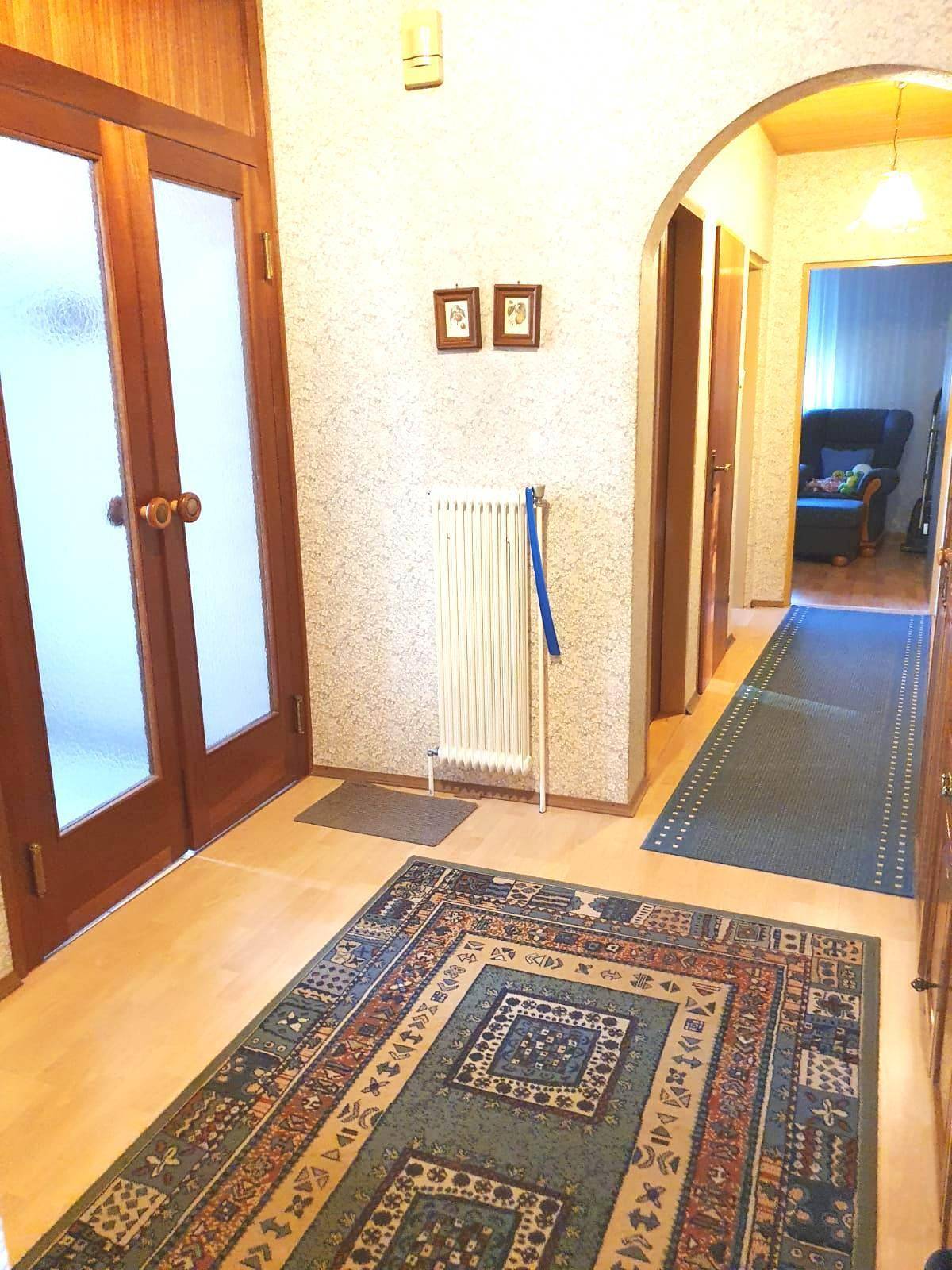 Heller Flur mit Holztüren, gemusterter Tapete und einem traditionellen Teppich auf Laminatboden.
