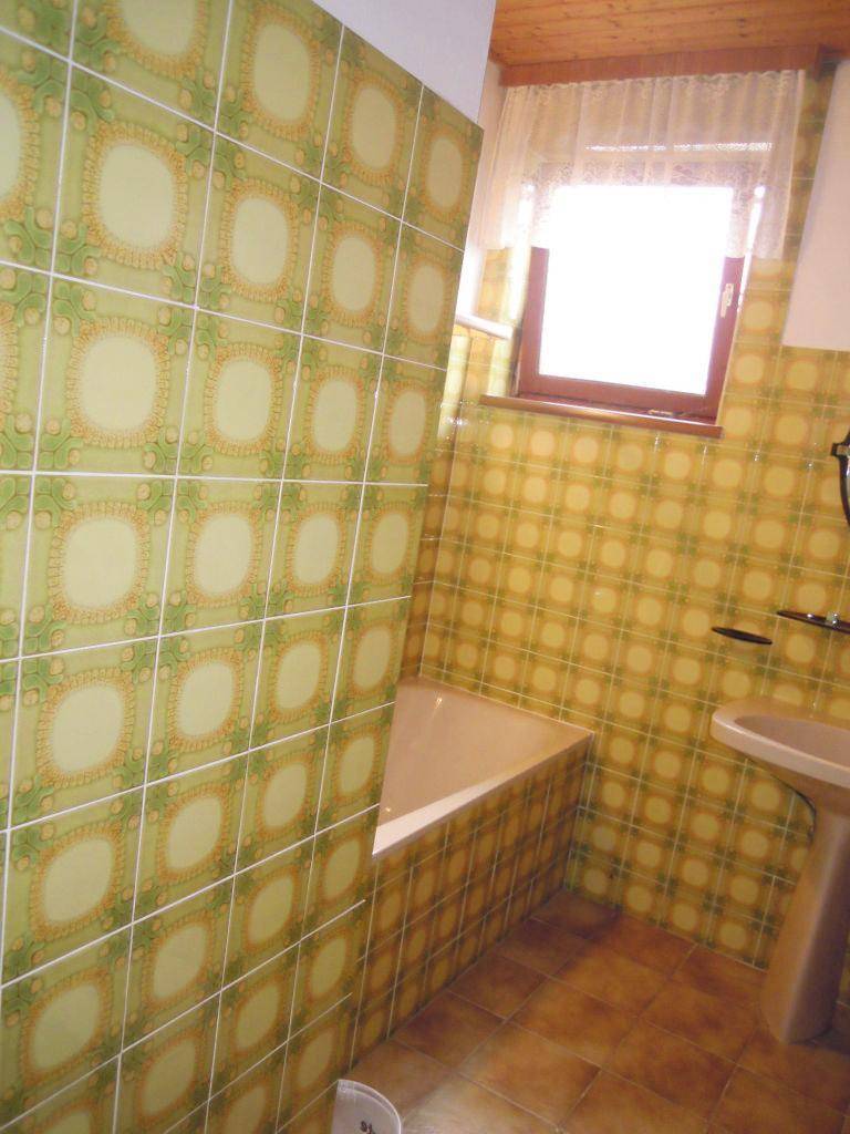 Badezimmer im Stil der 80er Jahre mit grünen und gelben Fliesen, Badewanne und Fenster.