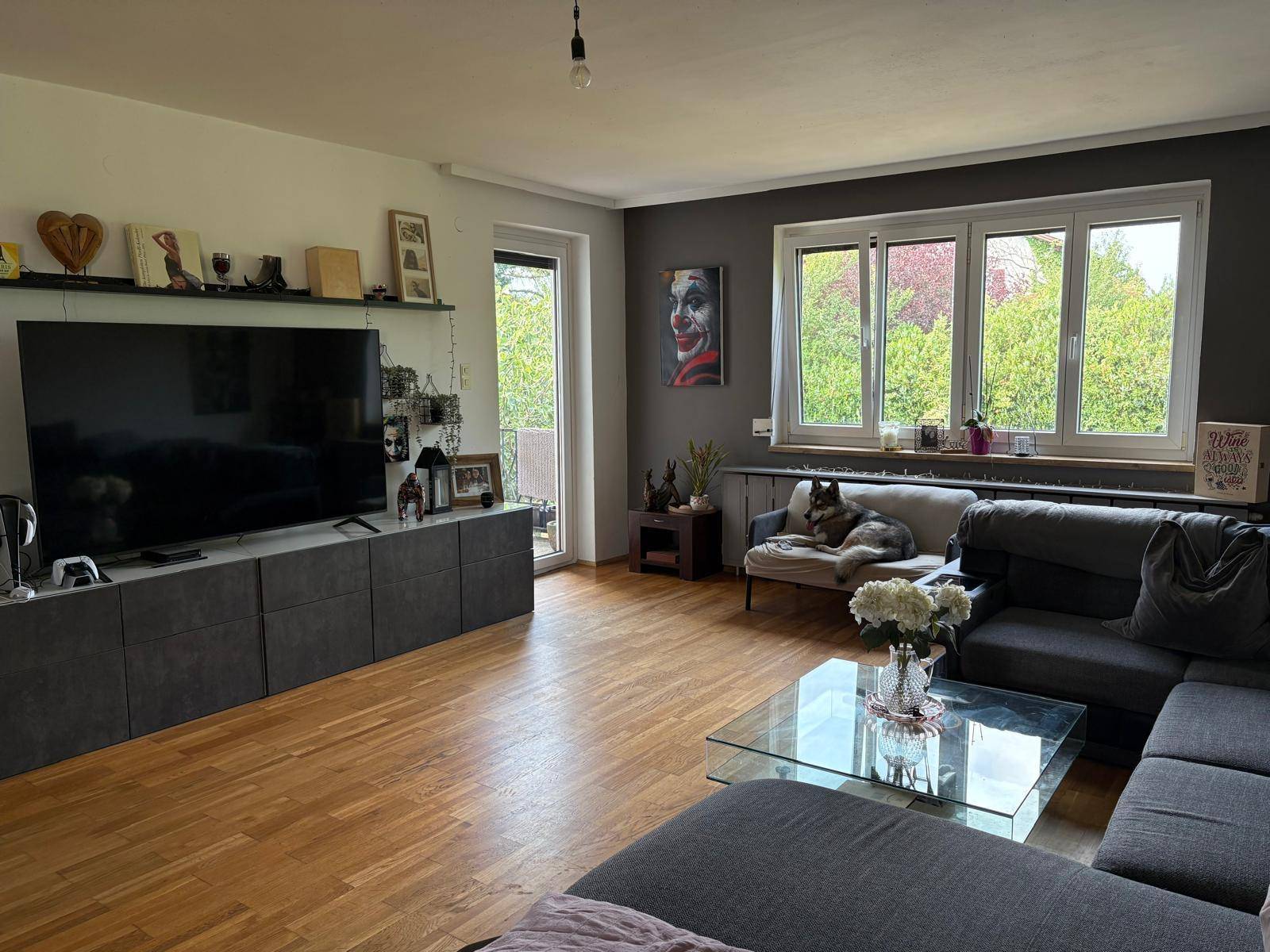 Geräumiges Wohnzimmer mit Holzboden, großem Sofa, Fernseher und Blick ins Grüne.