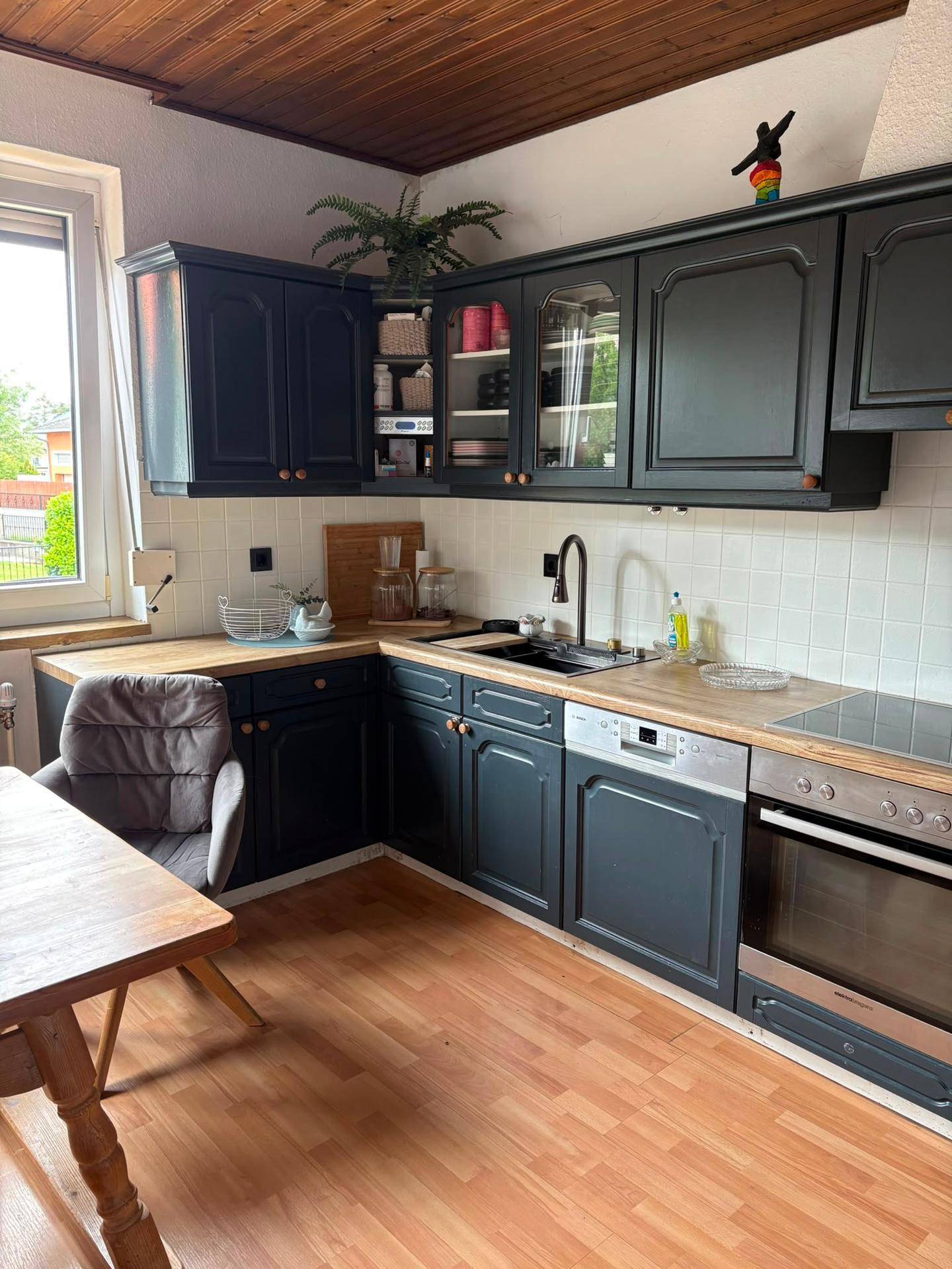 Moderne Küche mit dunkelgrauen Schränken, Holzarbeitsplatte, Spülmaschine und Fenster.