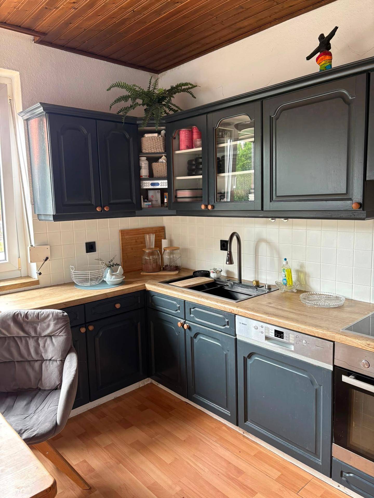 Moderne Küche mit dunkelgrauen Schränken, Holzarbeitsplatte, Spülmaschine und Fenster.