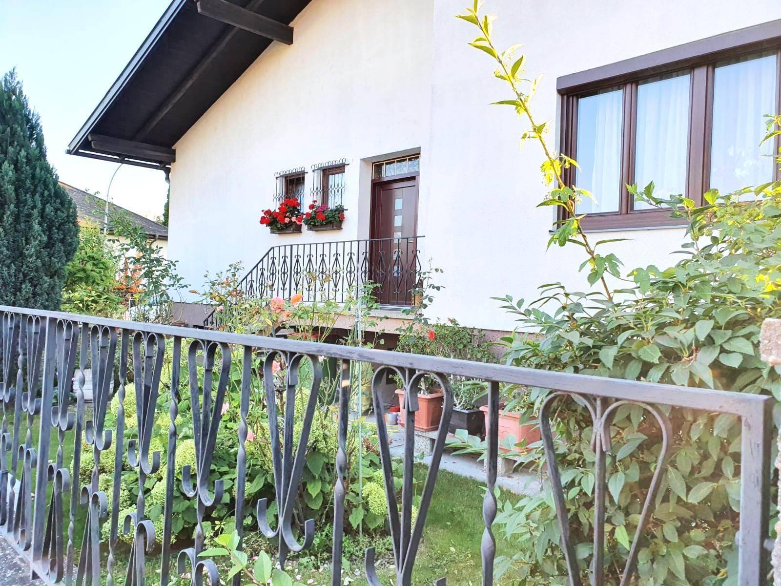 Vorderansicht des Hauses mit weißer Fassade, braunen Fenstern und einem gepflegten Vorgarten.