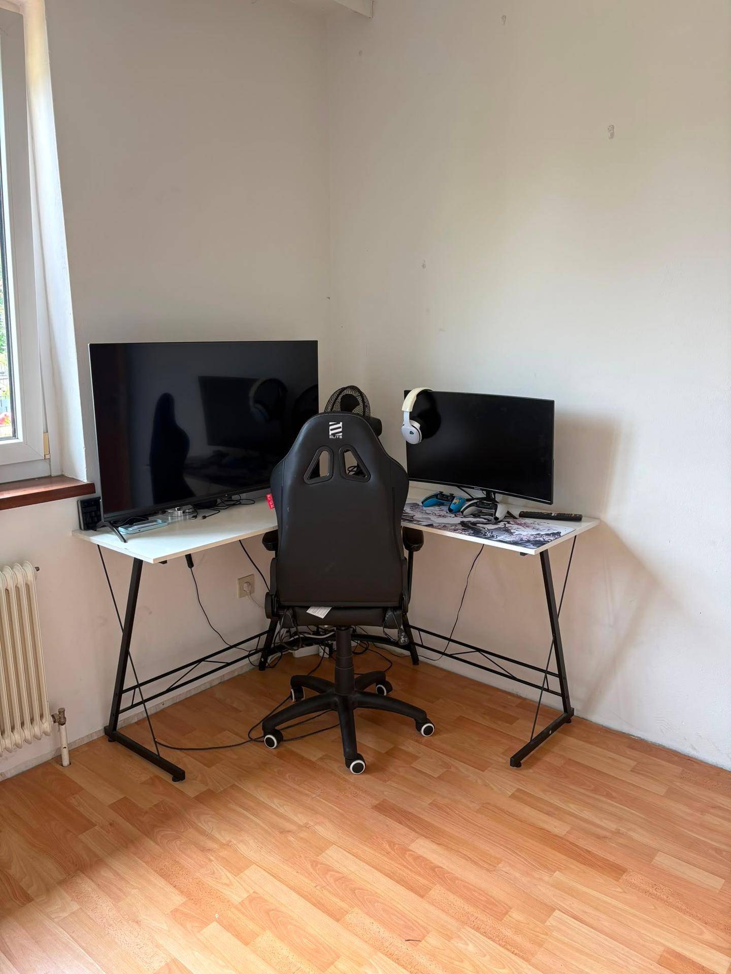 Arbeitszimmer mit Laminatboden, Eckschreibtisch, Gaming-Stuhl und zwei Monitoren.