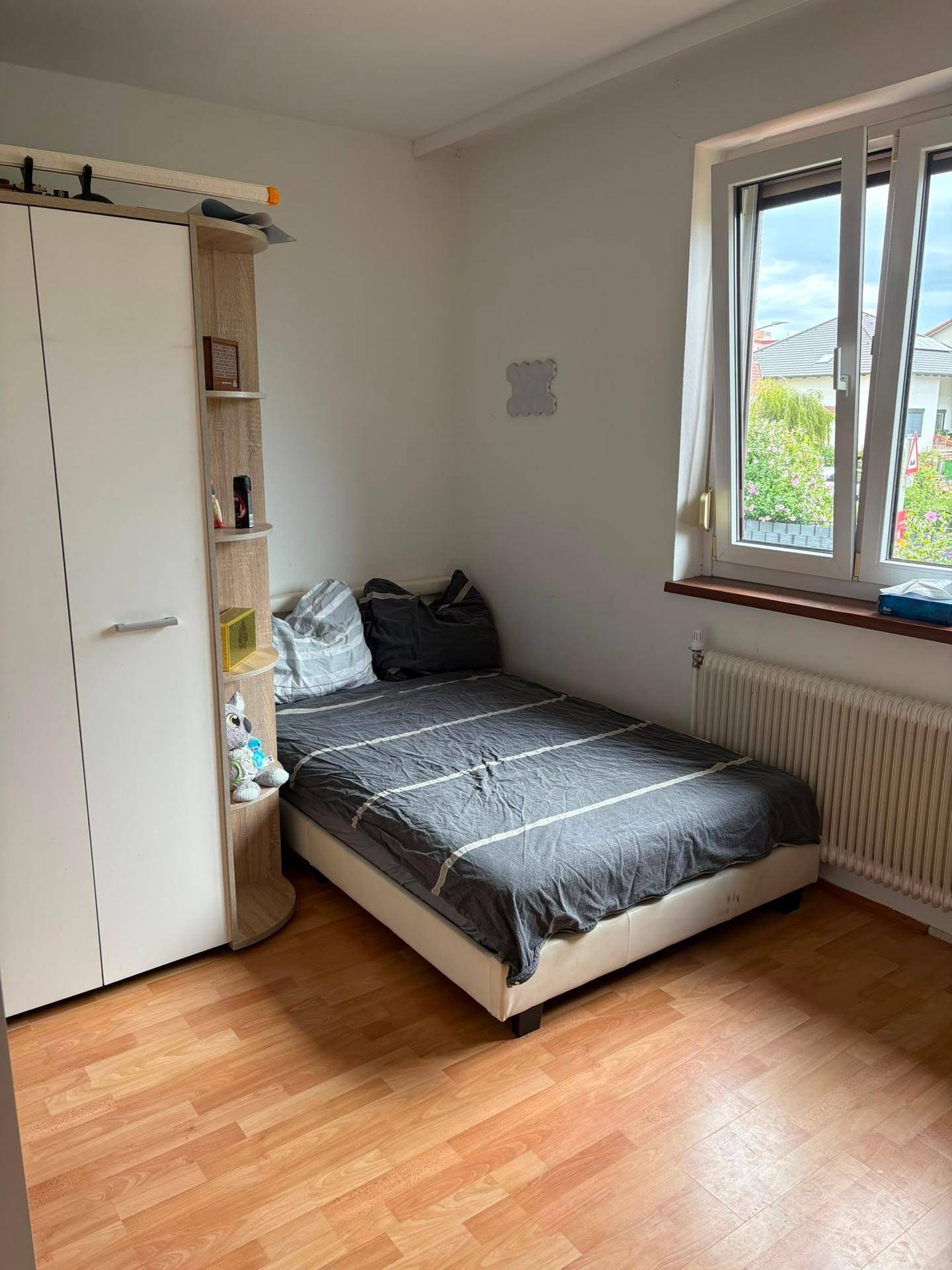 Schlafzimmer mit Laminatboden, Einzelbett, Kleiderschrank und Fenster mit Blick nach draußen.