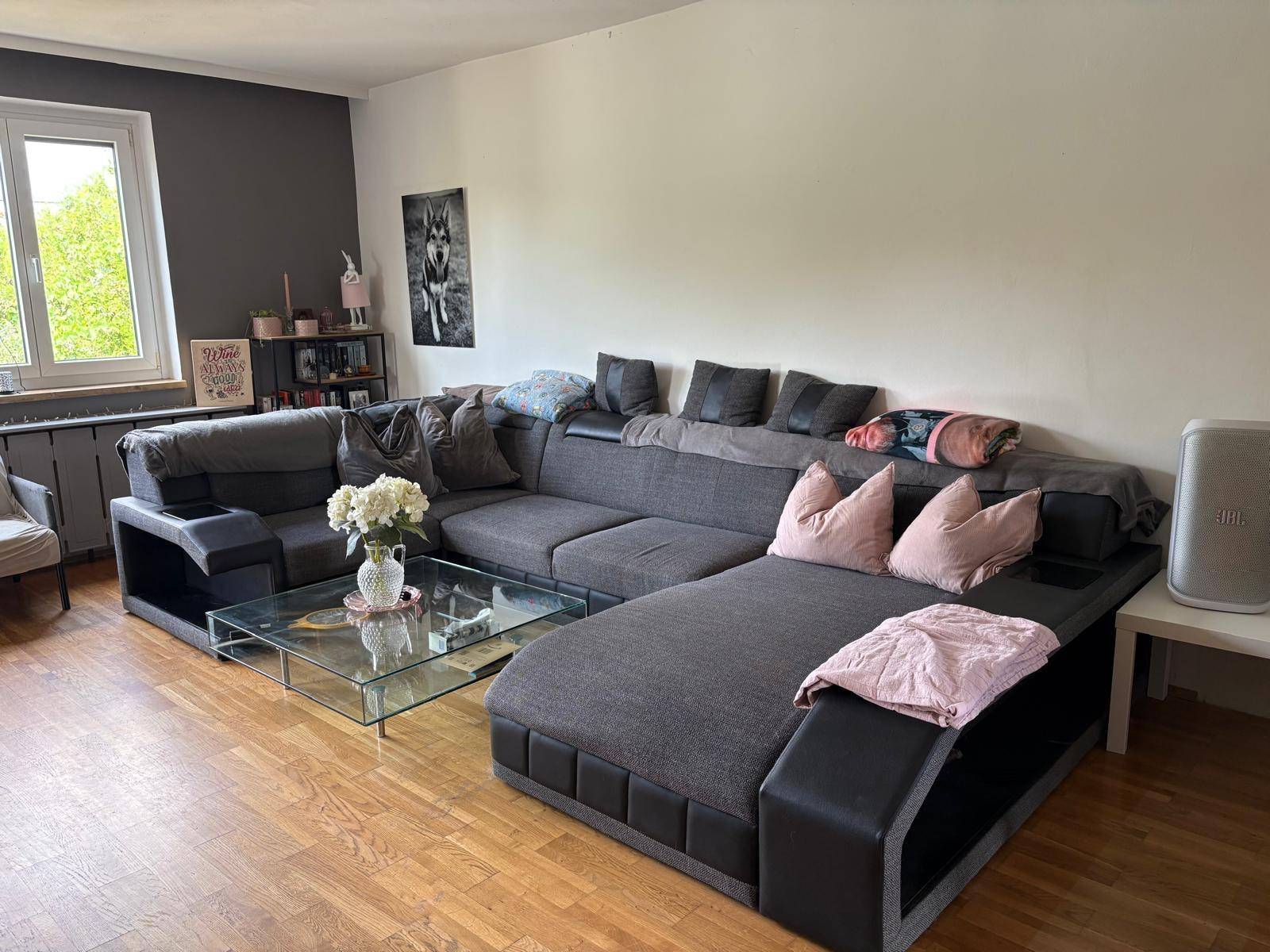Geräumiges Wohnzimmer mit großem Ecksofa, Holzboden und Fenster für viel Tageslicht.