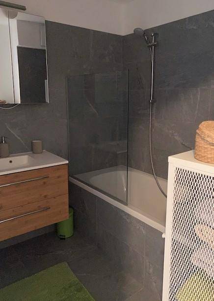 Badezimmer mit Badewanne, Duscharmatur und grauen Fliesen an Wänden und Boden.