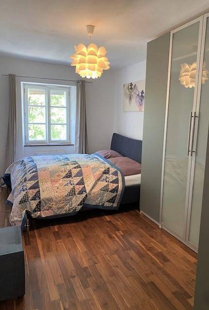 Schlafzimmer mit Doppelbett, Holzboden, Kleiderschrank und Fenster.