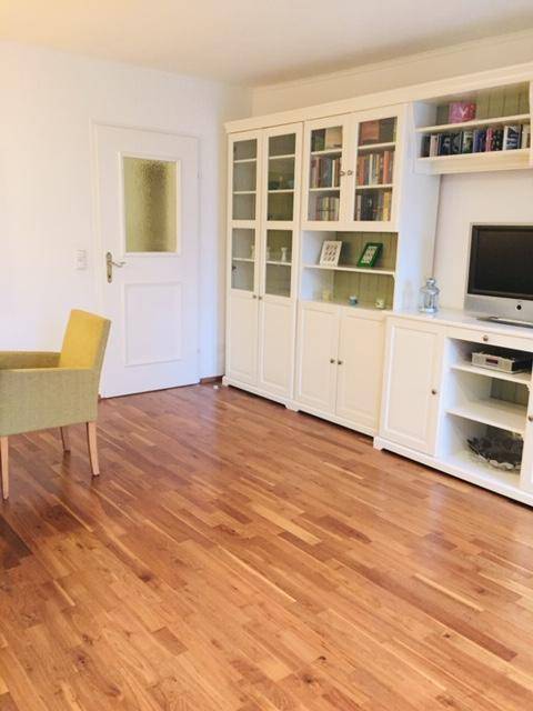 Wohnzimmer mit Holzboden, weißem Schrank und einer Tür mit Glaseinsatz.