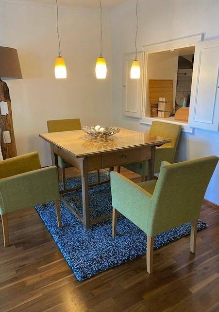Essbereich mit Holztisch, grünen Stühlen und Pendelleuchten über dem Tisch.