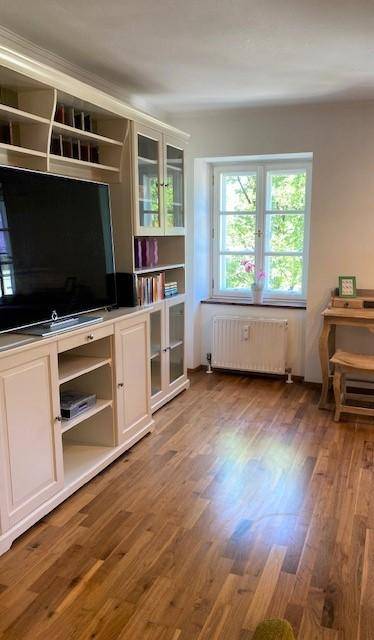 Helles Wohnzimmer mit Holzboden, weißem Bücherregal und Fernseher.