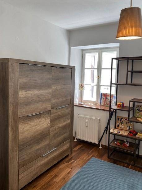Kinderzimmer mit Holzschrank, Regal und Fenster mit Blick nach draußen.