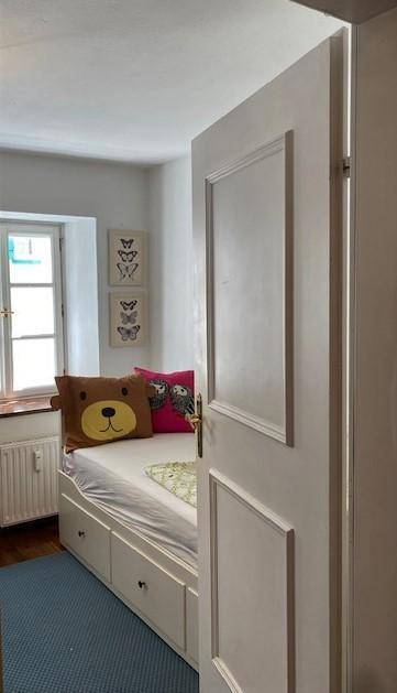 Kinderzimmer mit Einzelbett, Holzboden und Fenster mit Blick ins Grüne.