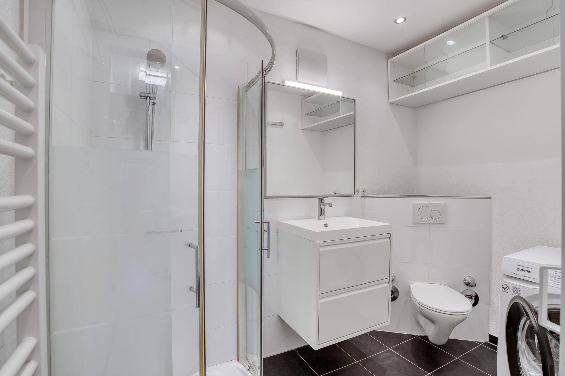 Helles Badezimmer mit Duschkabine, WC, Waschbecken und integrierter Waschmaschine.