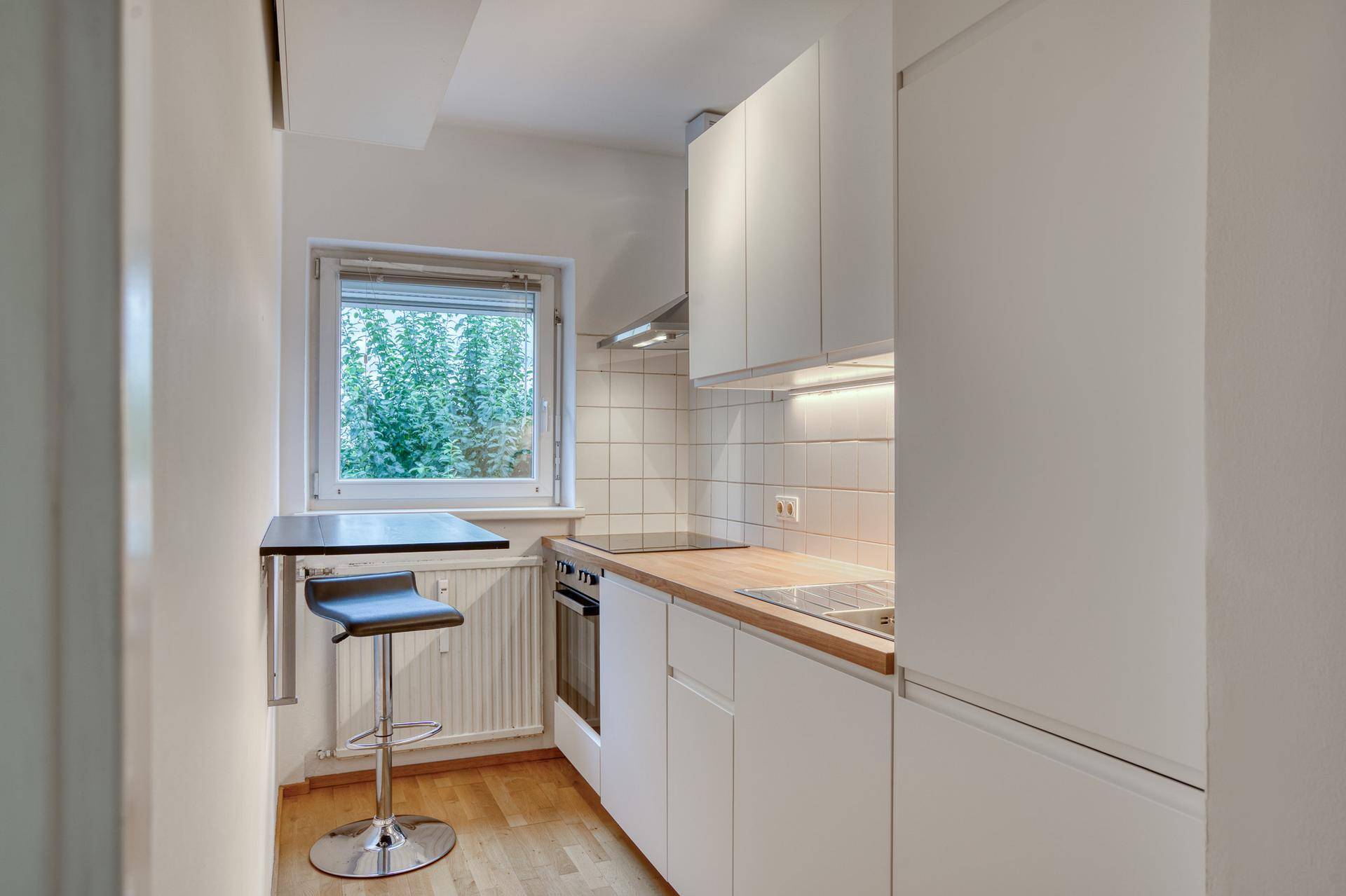 Kompakte Küche mit Fenster, Einbaugeräten und einer kleinen Frühstücksbar.