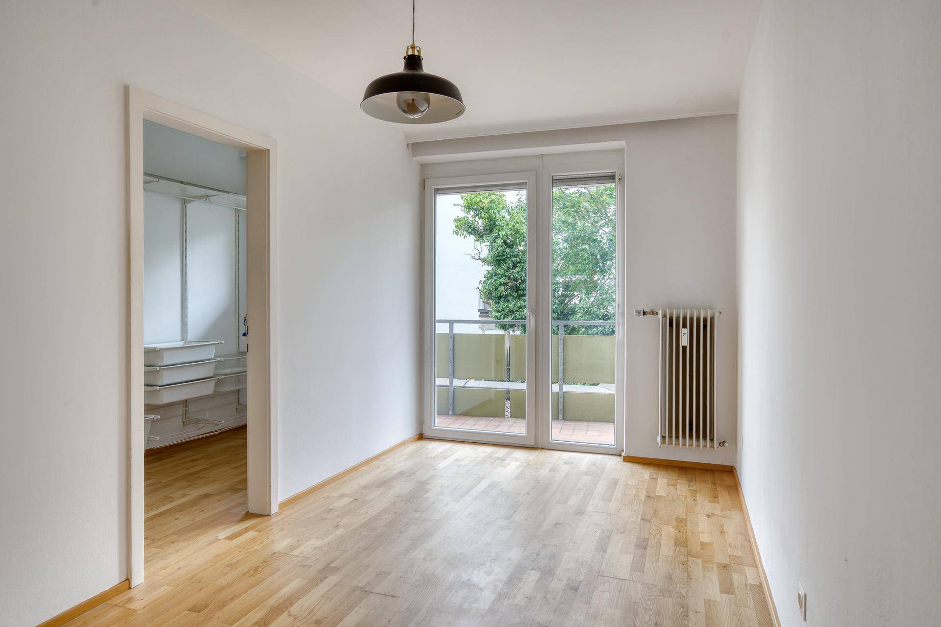 Helles Schlafzimmer mit Parkettboden, Balkonzugang und offenem Zugang zu einem Ankleidebereich.