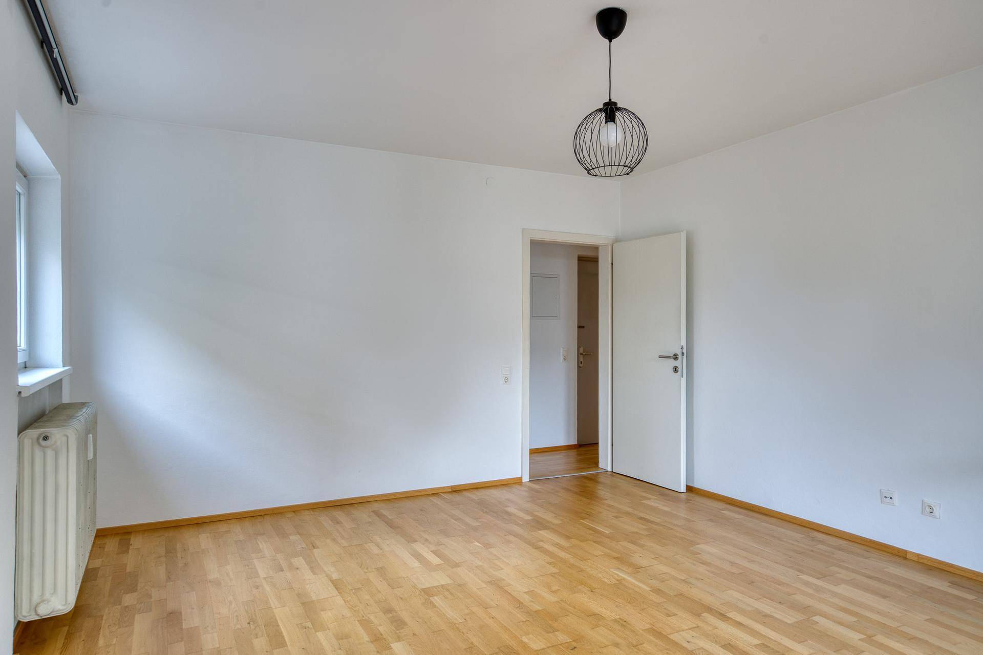 Heller Wohnraum mit Parkettboden und einer Tür, die zu einem weiteren Zimmer führt.
