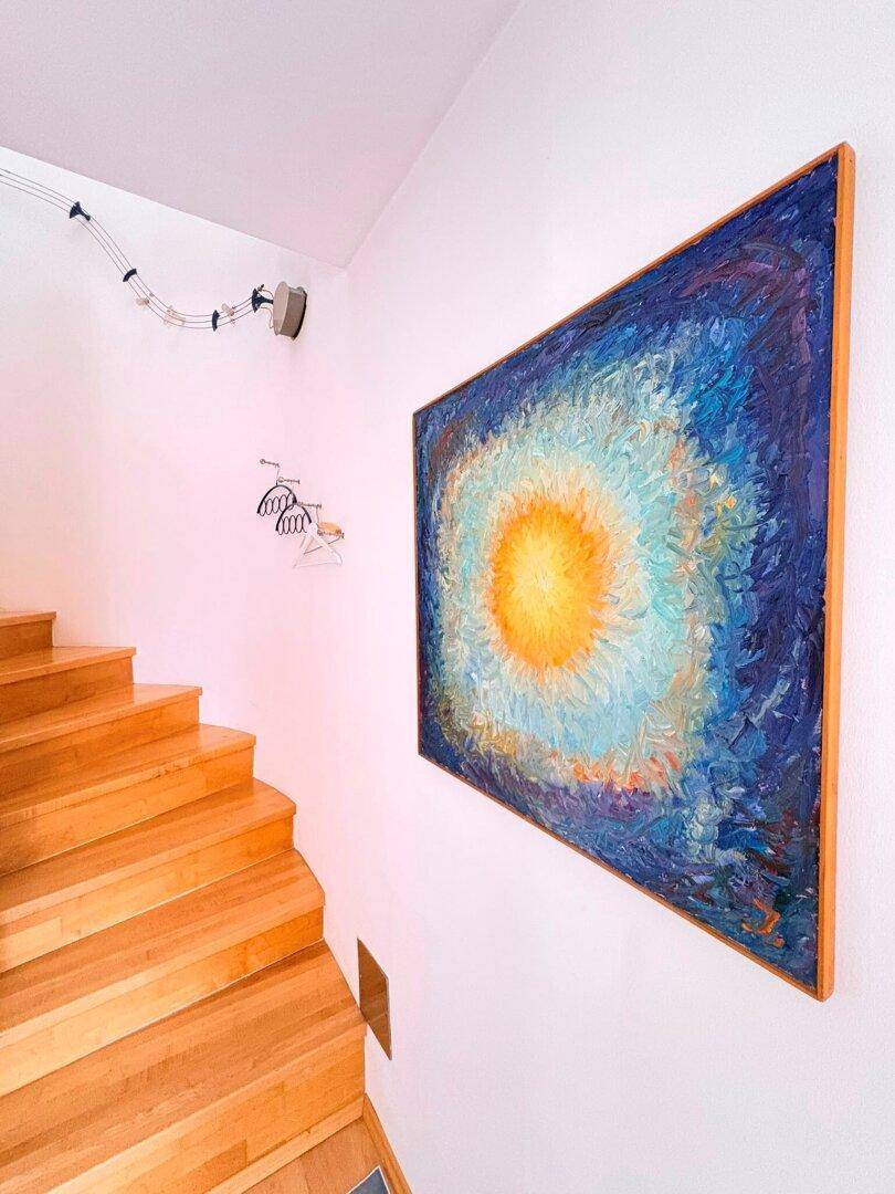 Holztreppe mit einem großen, farbenfrohen Kunstwerk an der weißen Wand.