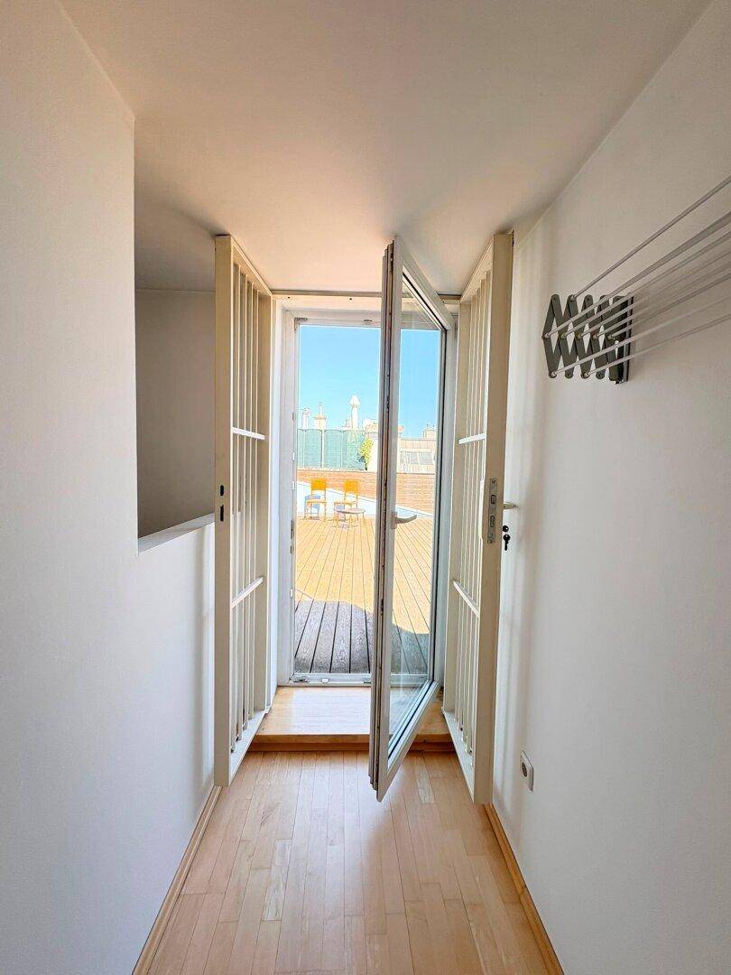 Heller Flur mit Holzboden, der zu einer sonnigen Dachterrasse mit Stadtblick führt.
