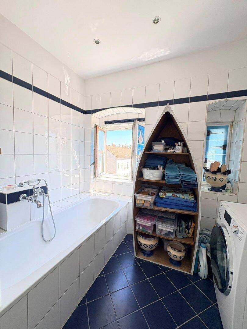 Helles Badezimmer mit Badewanne, blauen Fliesen, Fenster und einer Waschmaschine.