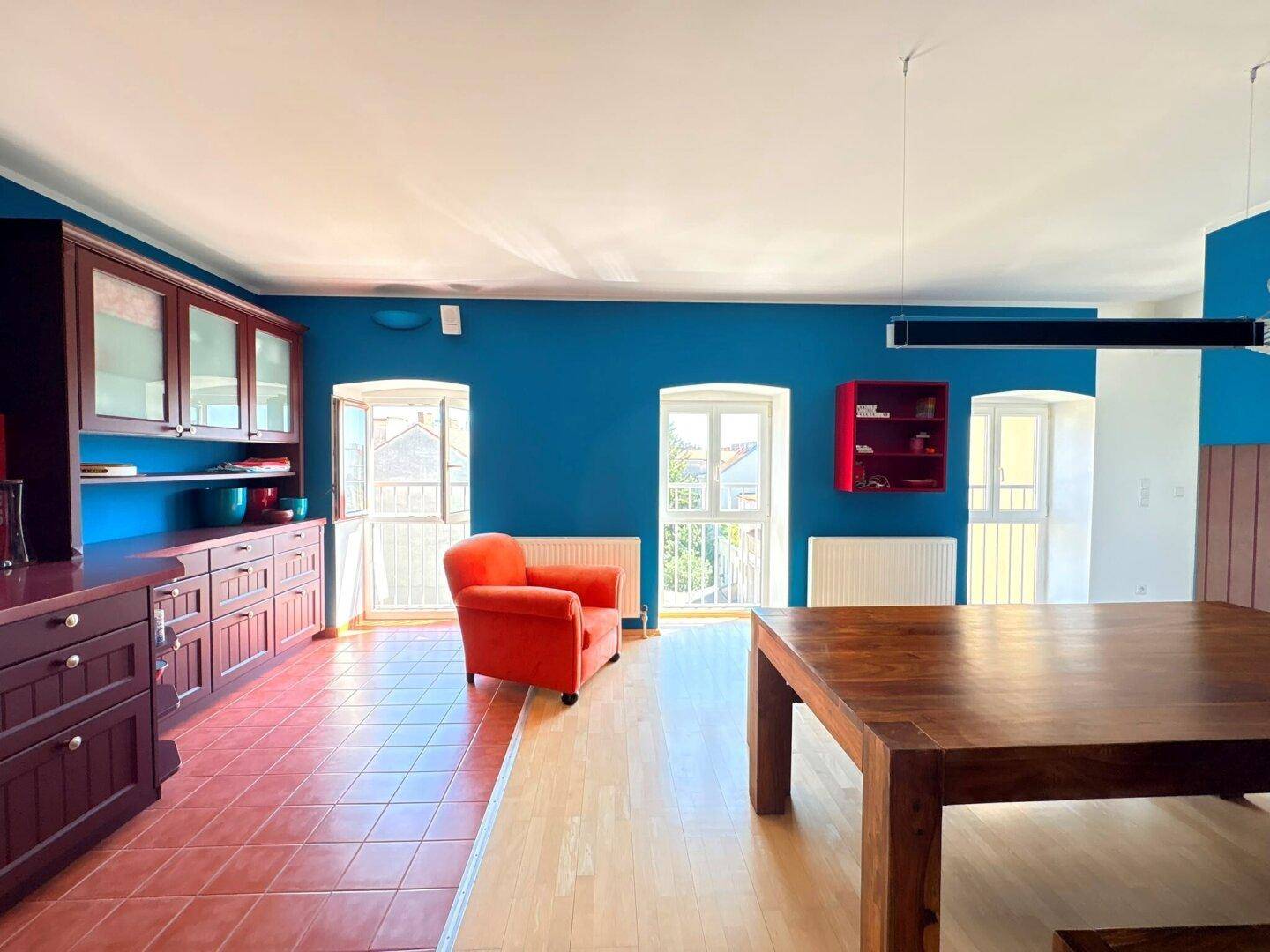 Farbenfroher Wohn- und Essbereich mit blauen Wänden, Holztisch und Zugang zu französischen Balkonen.