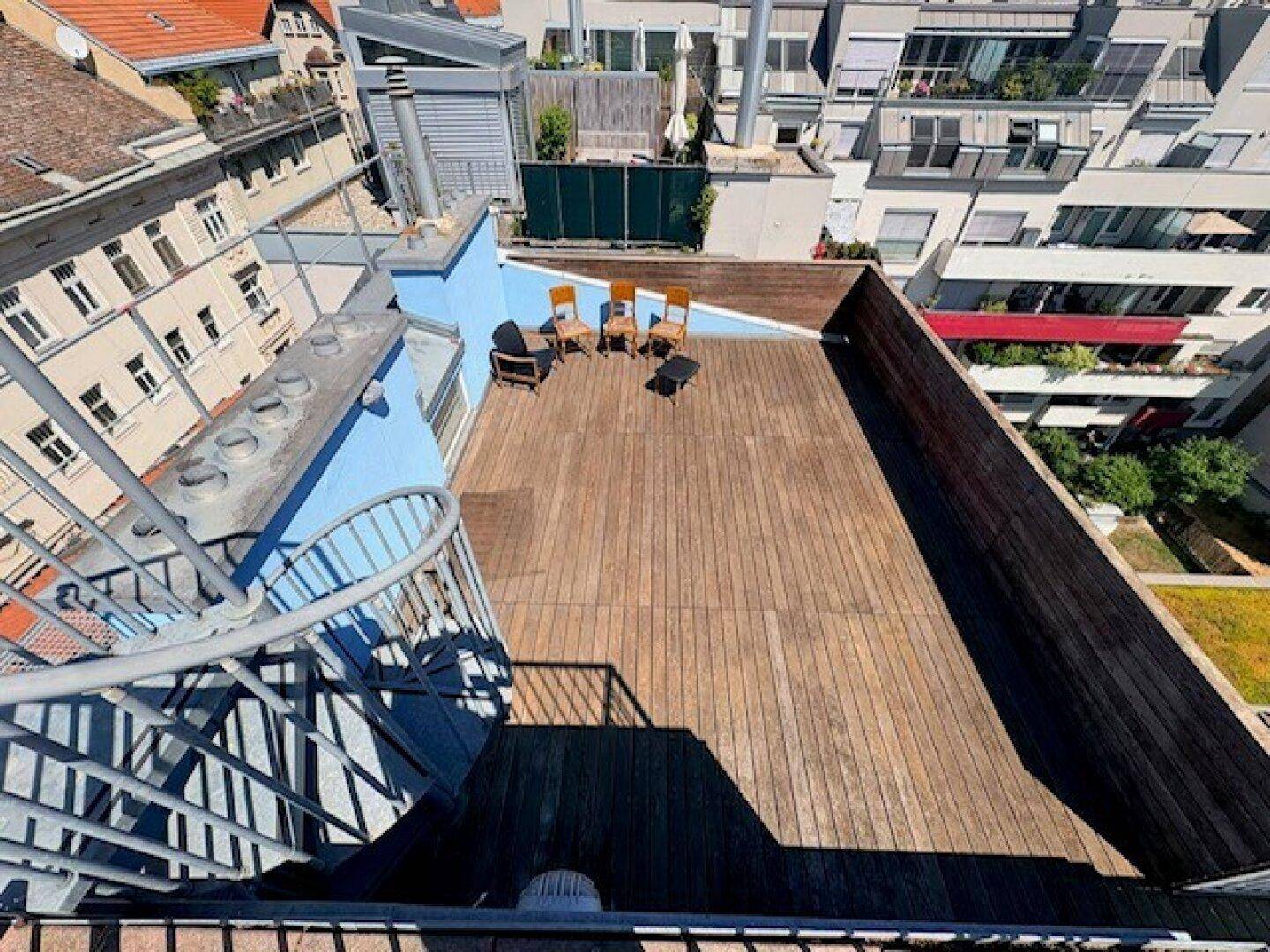 Geräumige Dachterrasse aus Holz mit Sitzgelegenheiten und Blick auf die umliegenden Gebäude.