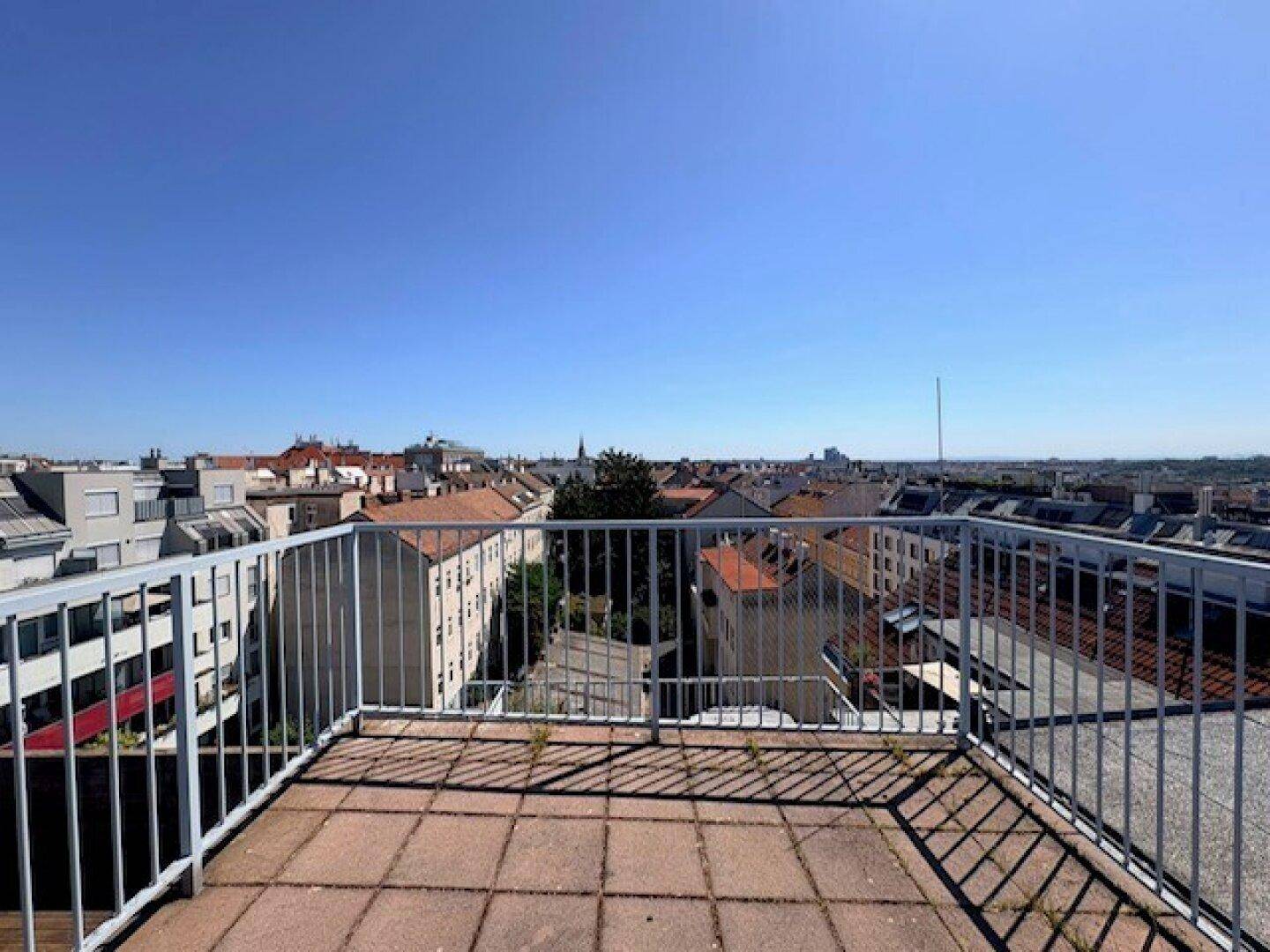 Dachbalkon mit Metallgeländer und weitem Blick über die Dächer der Stadt.