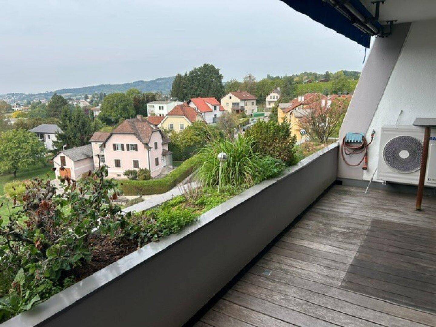 Geräumiger Balkon mit Holzboden, Pflanzen und weitem Blick über die Umgebung.