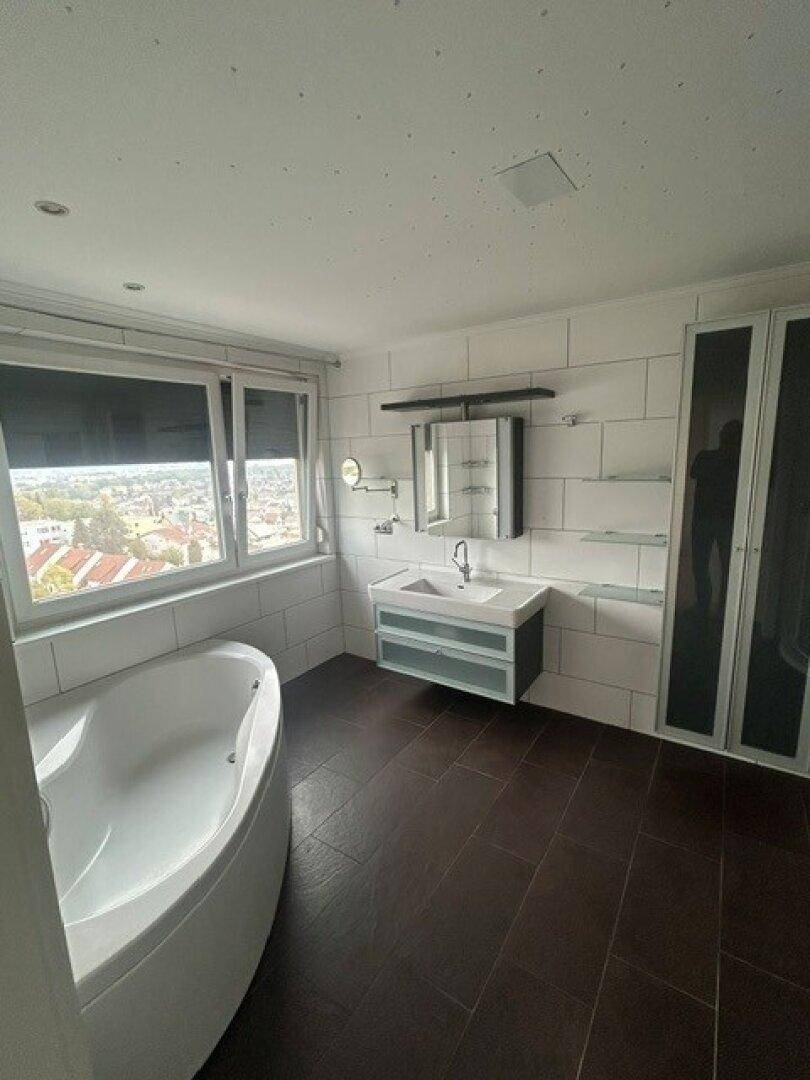 Helles Badezimmer mit großer Badewanne, Einzelwaschbecken und Fenster mit Ausblick.