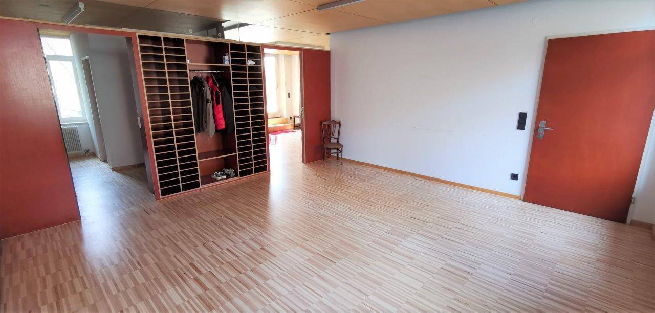 Geräumiger Innenraum mit Holzparkett, einer offenen Regalwand und roten Türen.