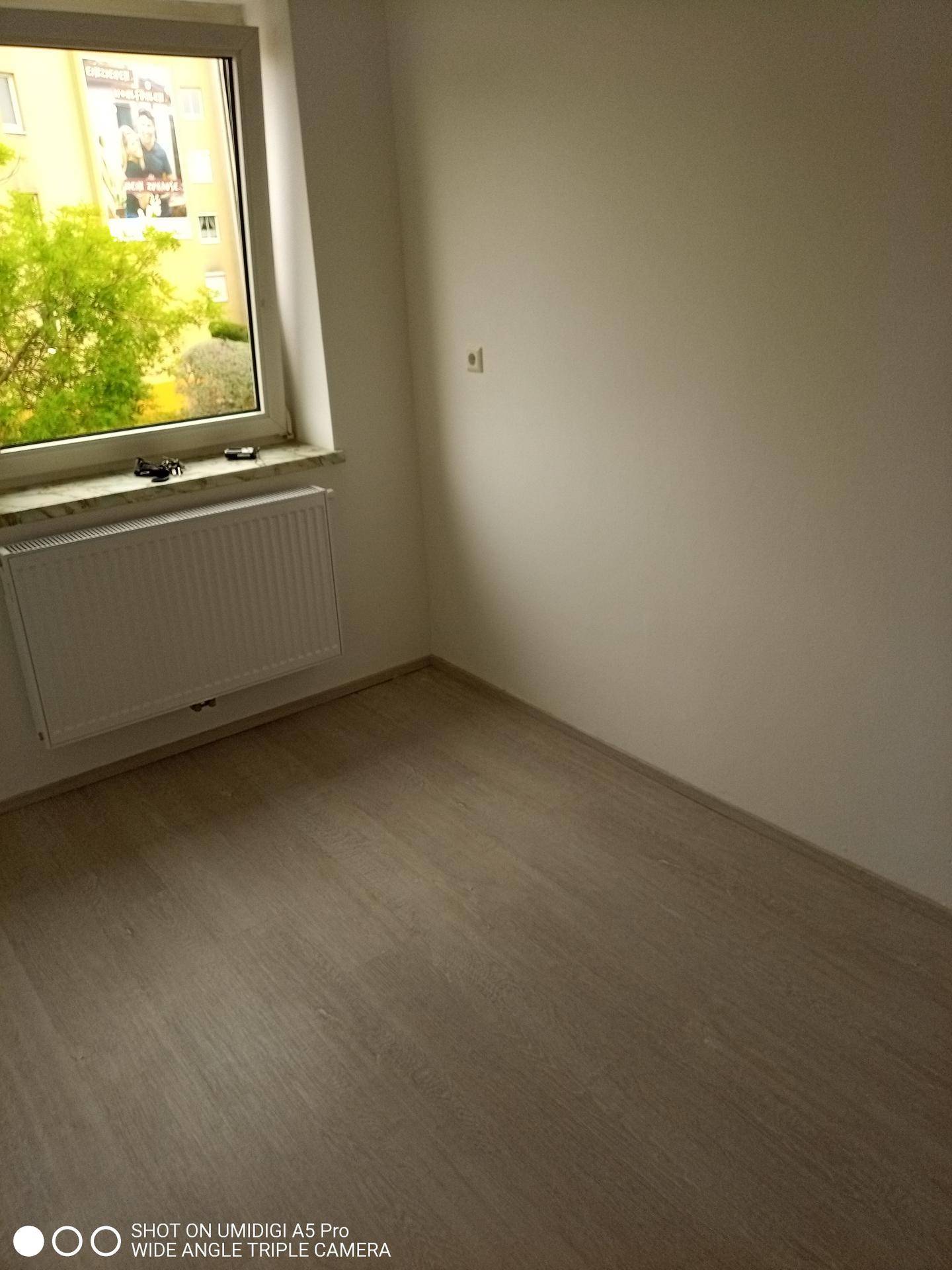 Helles Zimmer mit Laminatboden, Fenster und Blick ins Grüne.