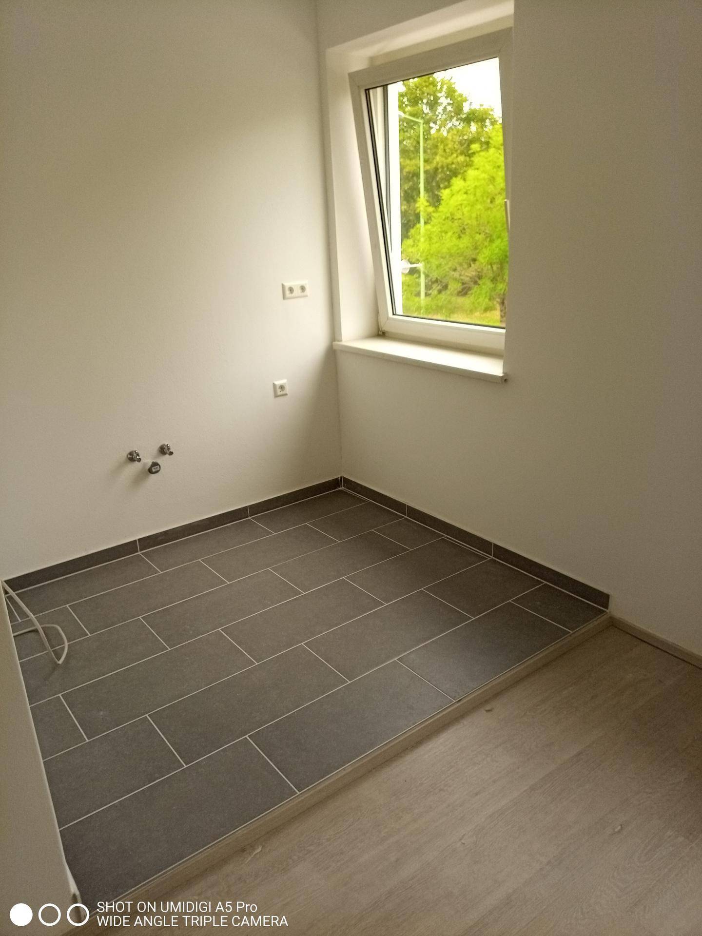 Kleiner Raum mit Fliesenboden, Fenster und Anschlüssen, ideal als Abstellraum.