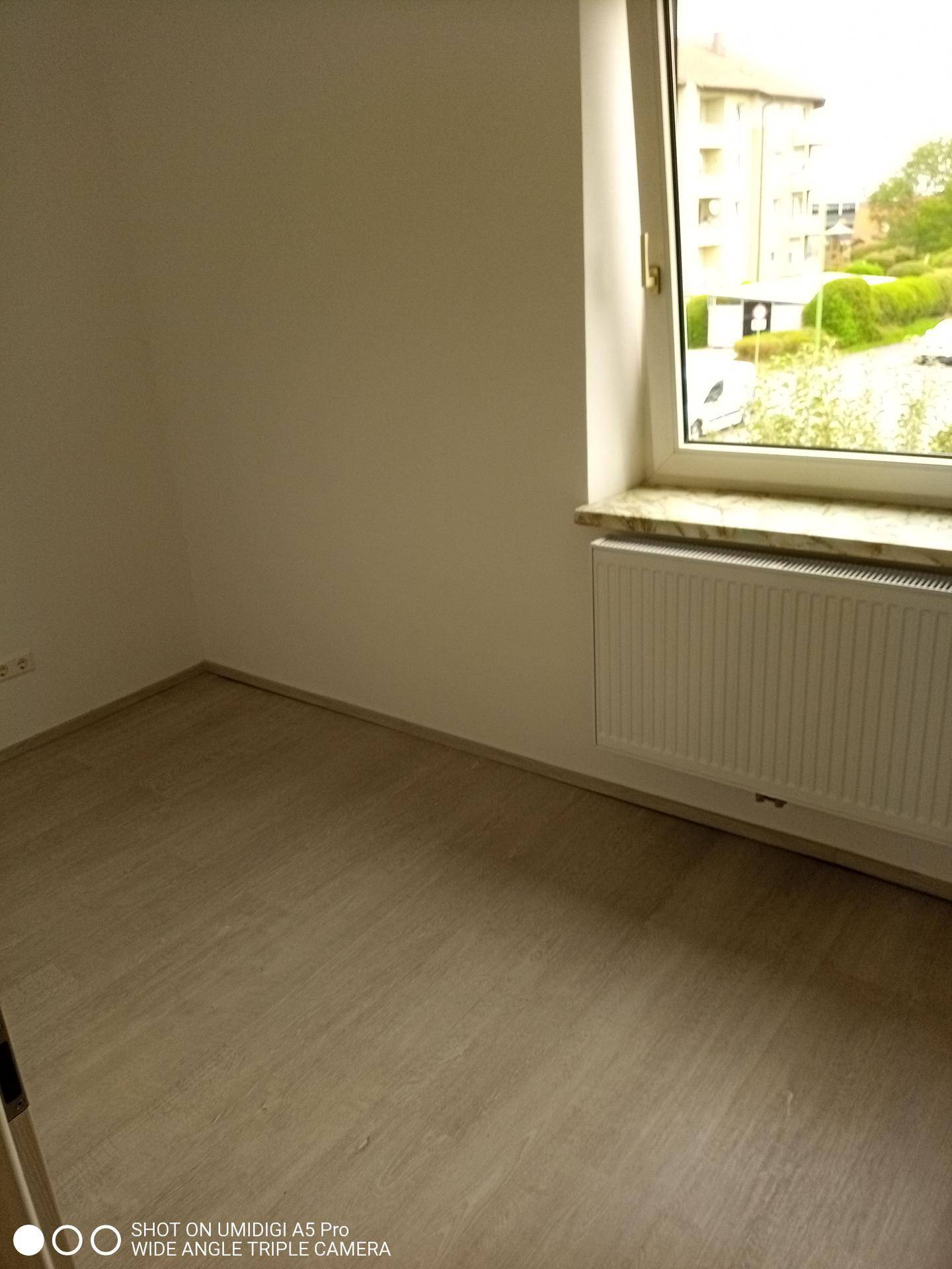 Helles Zimmer mit Laminatboden, Fenster und Blick ins Grüne.