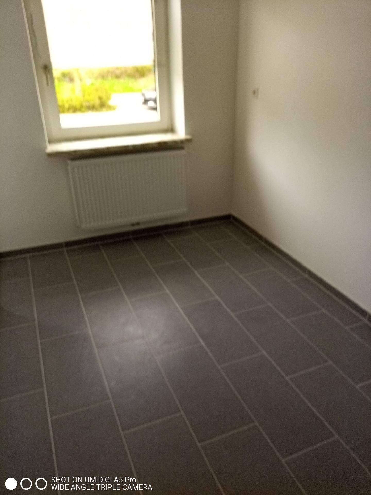 Helles Zimmer mit Fliesenboden, Fenster und Blick ins Grüne.