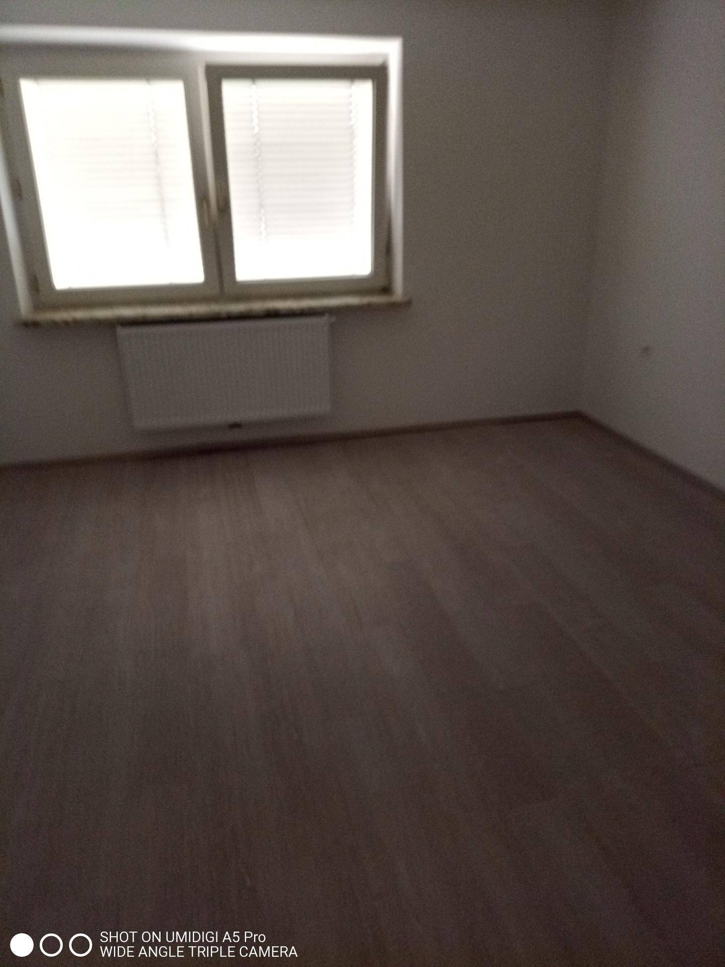 Leeres Zimmer mit Laminatboden, Fenster und Heizkörper, ideal als Schlafzimmer.