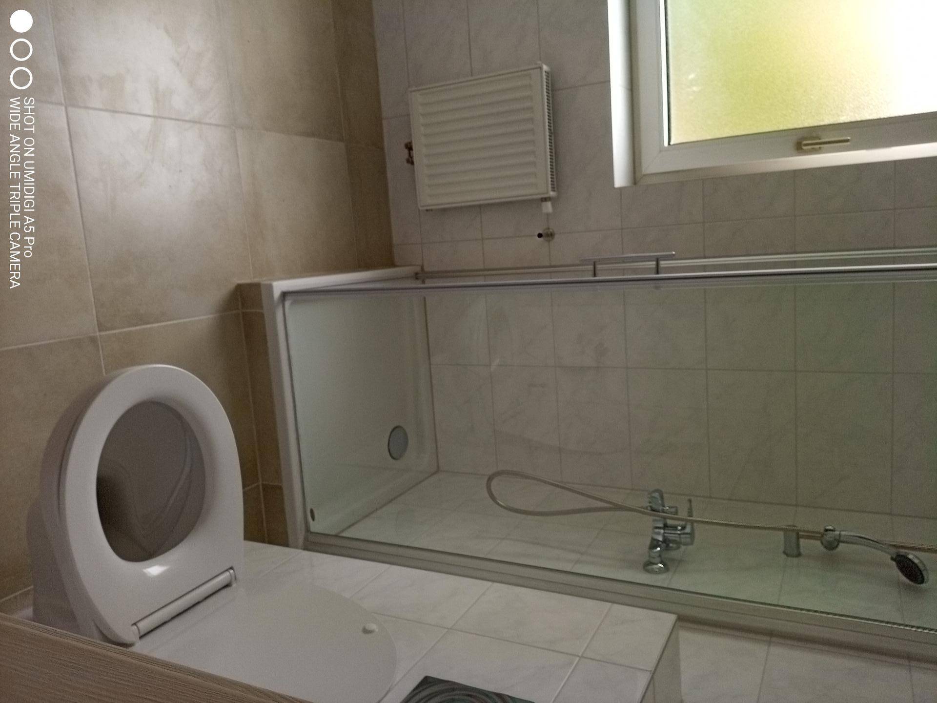Badezimmer mit WC, Dusch-Badewannen-Kombination und hellen Fliesen.