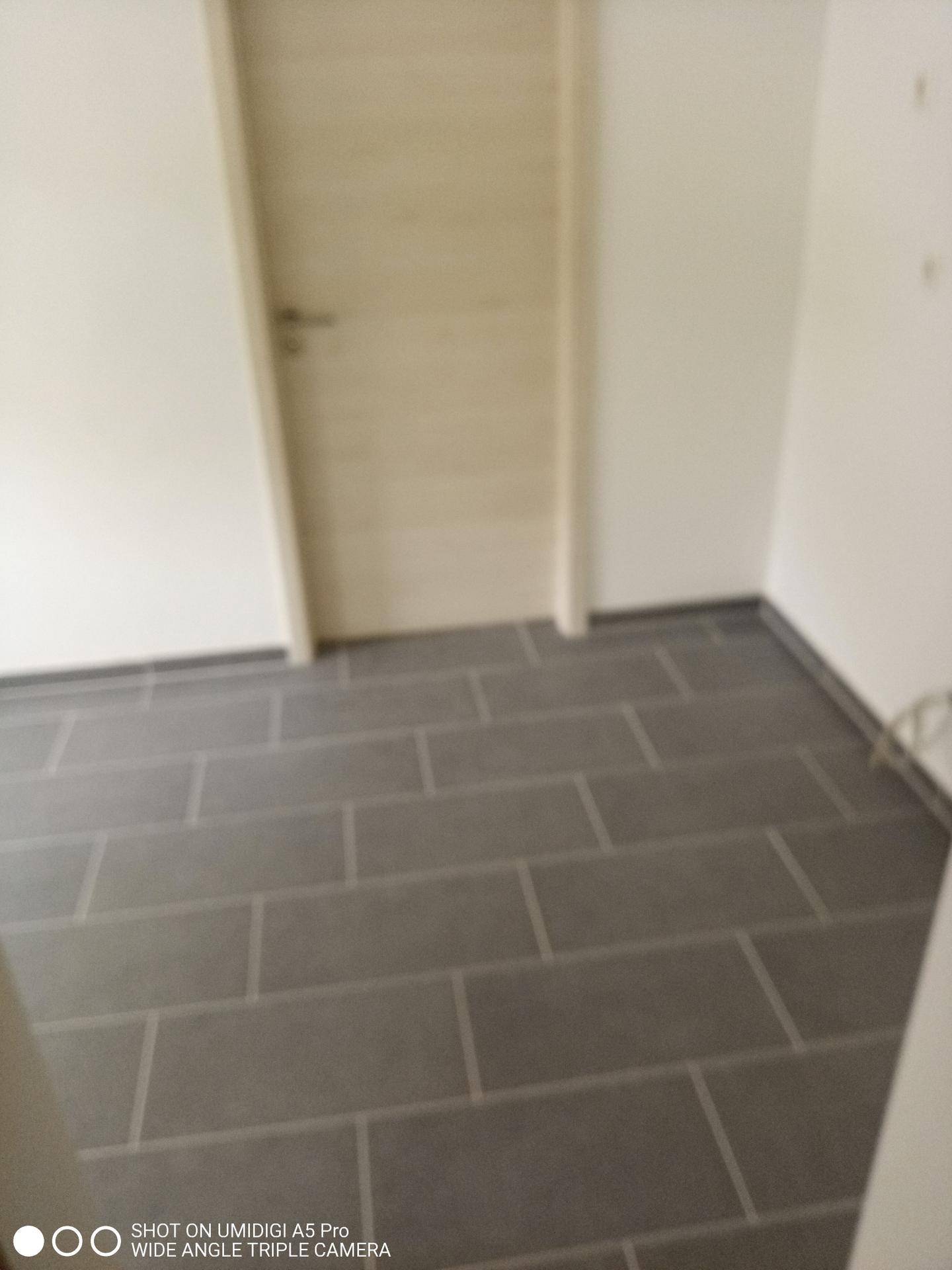 Heller Raum mit modernen grauen Fliesen und einer schlichten Holztür.