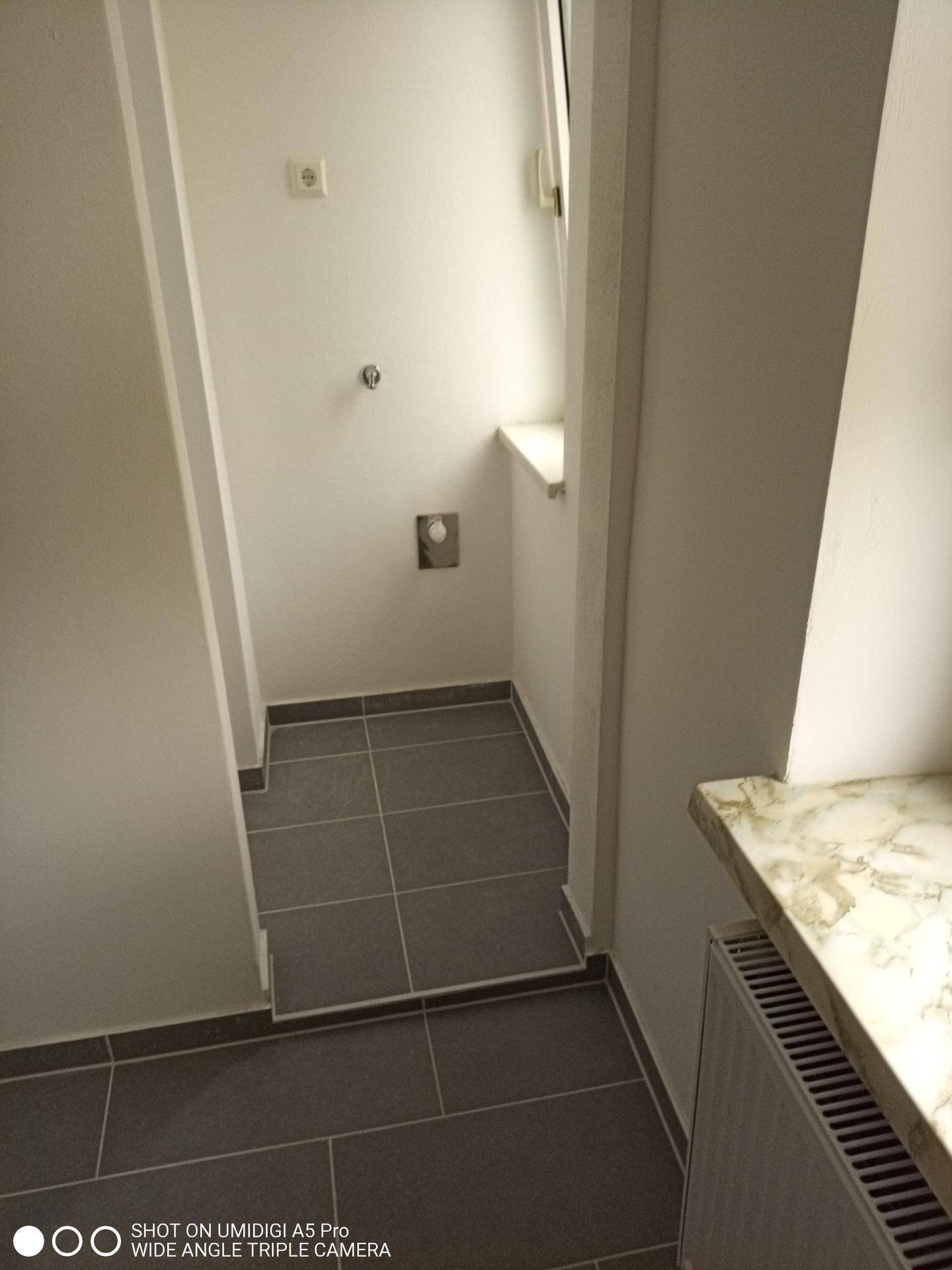 Praktischer Hauswirtschaftsraum mit Fliesenboden, Fenster und Anschlüssen für Waschmaschine.