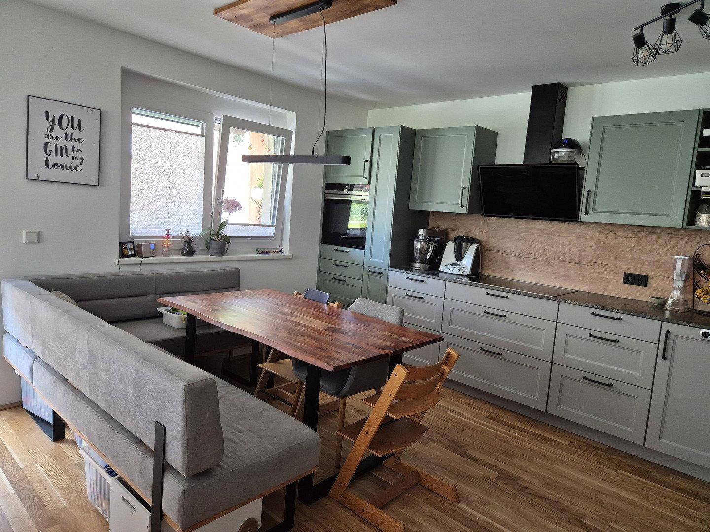 Moderne Wohnküche mit grauen Schränken, Holzakzenten und Essbereich.