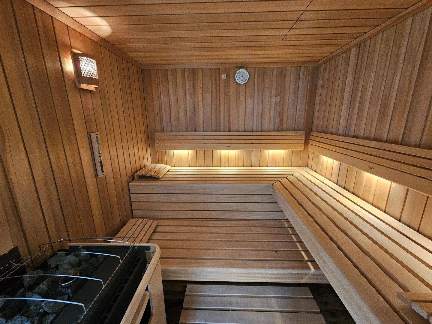 Geräumige Holzsauna mit mehreren Bänken und traditionellem Saunaofen für Wellnessmomente.