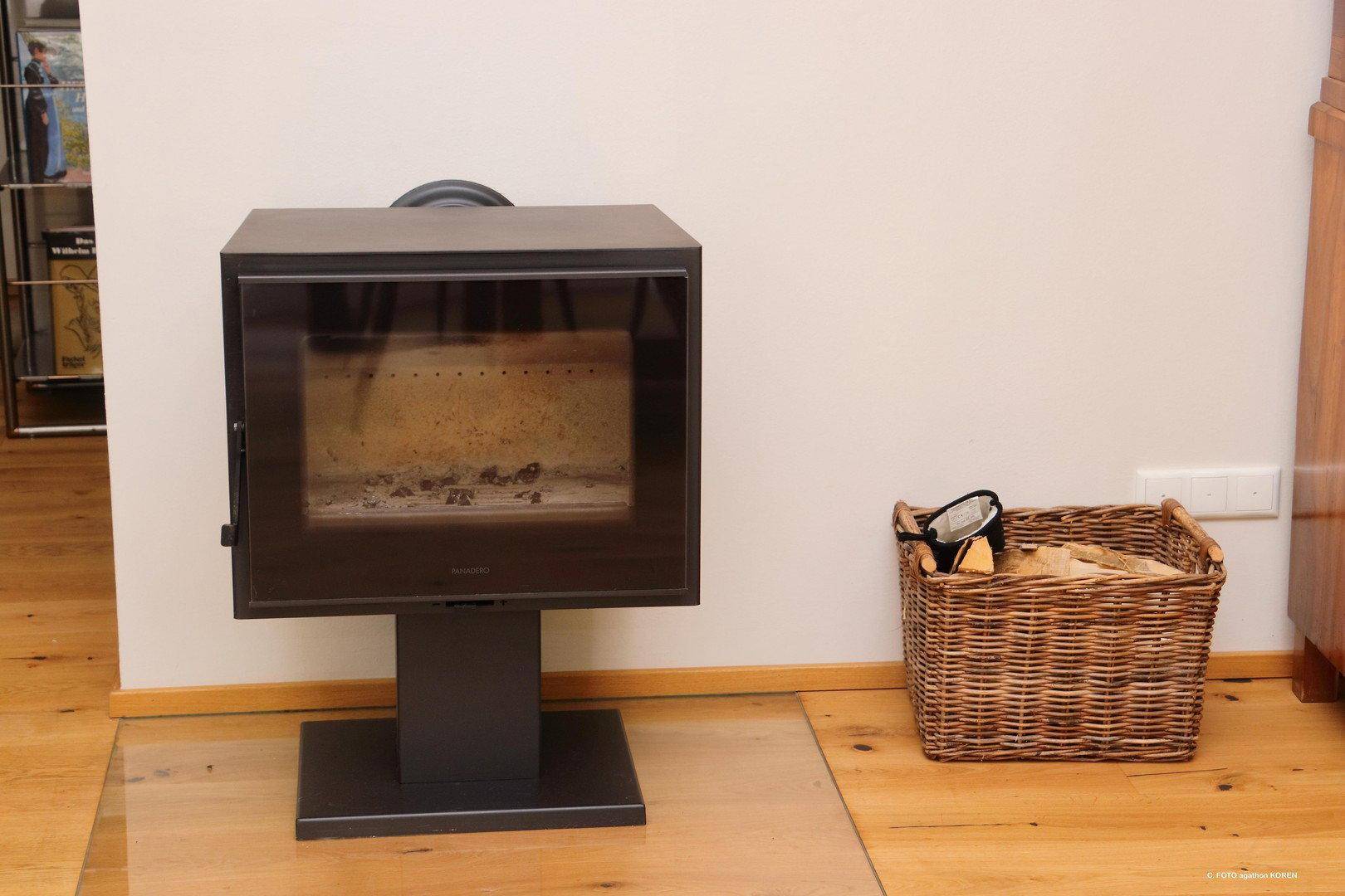 Moderner Holzofen im Wohnbereich, umgeben von Holzboden und einem Korb mit Brennholz.