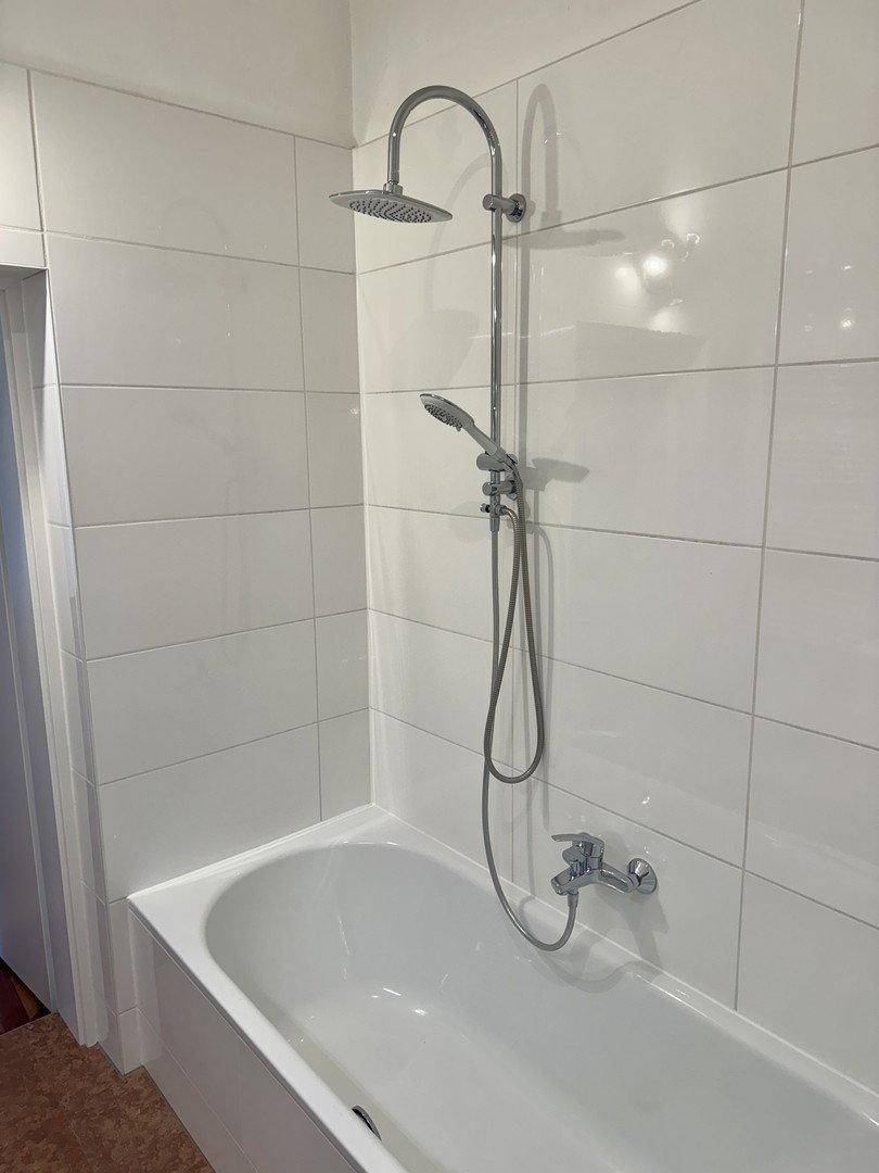 Badezimmer mit Badewanne und moderner Regendusche, komplett gefliest in Weiß.