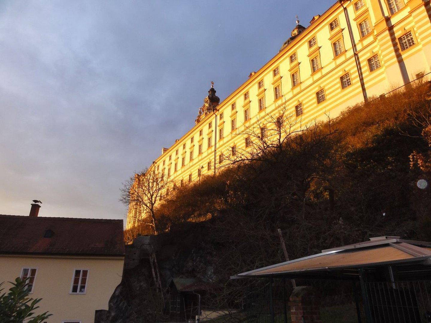 Majestätisches historisches Gebäude auf einem Hügel, von der Abendsonne beleuchtet, mit weitem Blick in die Landschaft.