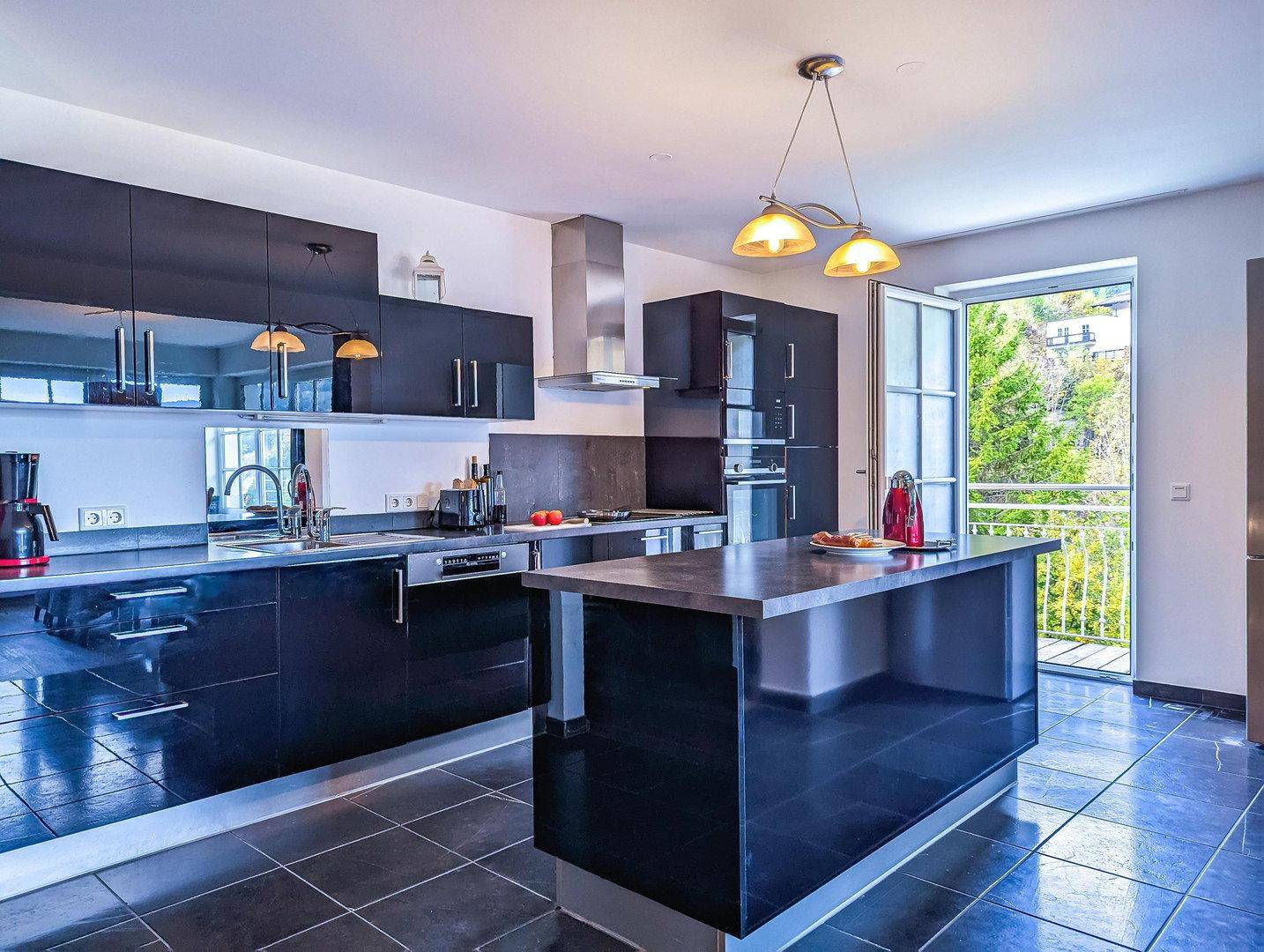 Hochglanzküche in Schwarz mit modernen Geräten, Kochinsel und Zugang zu einem kleinen Balkon.