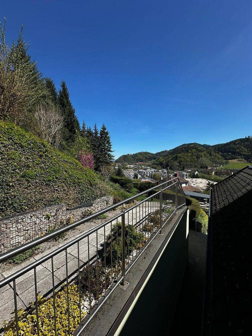 Balkon mit Metallgeländer und weitem Blick über die hügelige Landschaft und Siedlung.