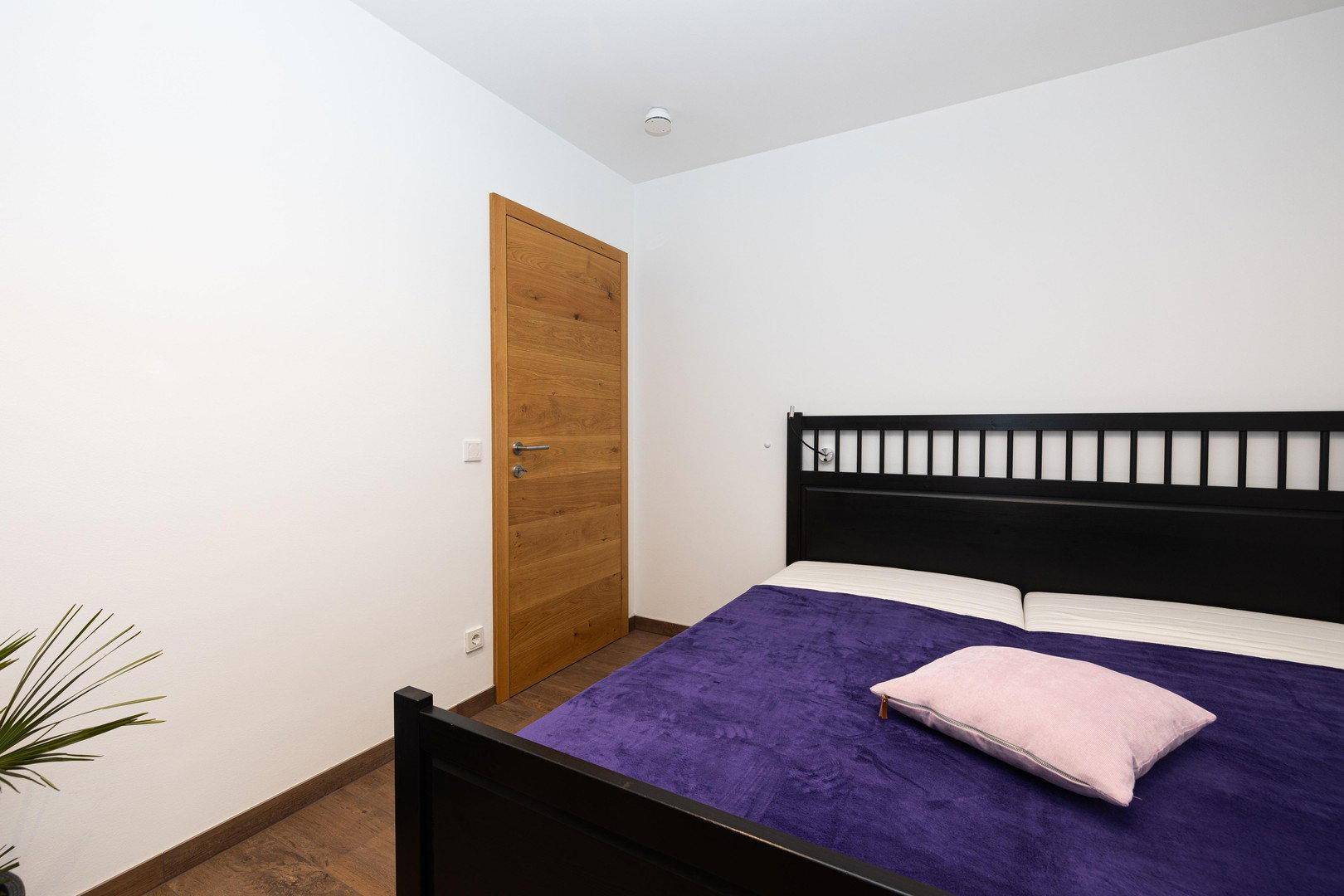 Einfaches Schlafzimmer mit Doppelbett und Holztür, das eine ruhige Atmosphäre bietet.